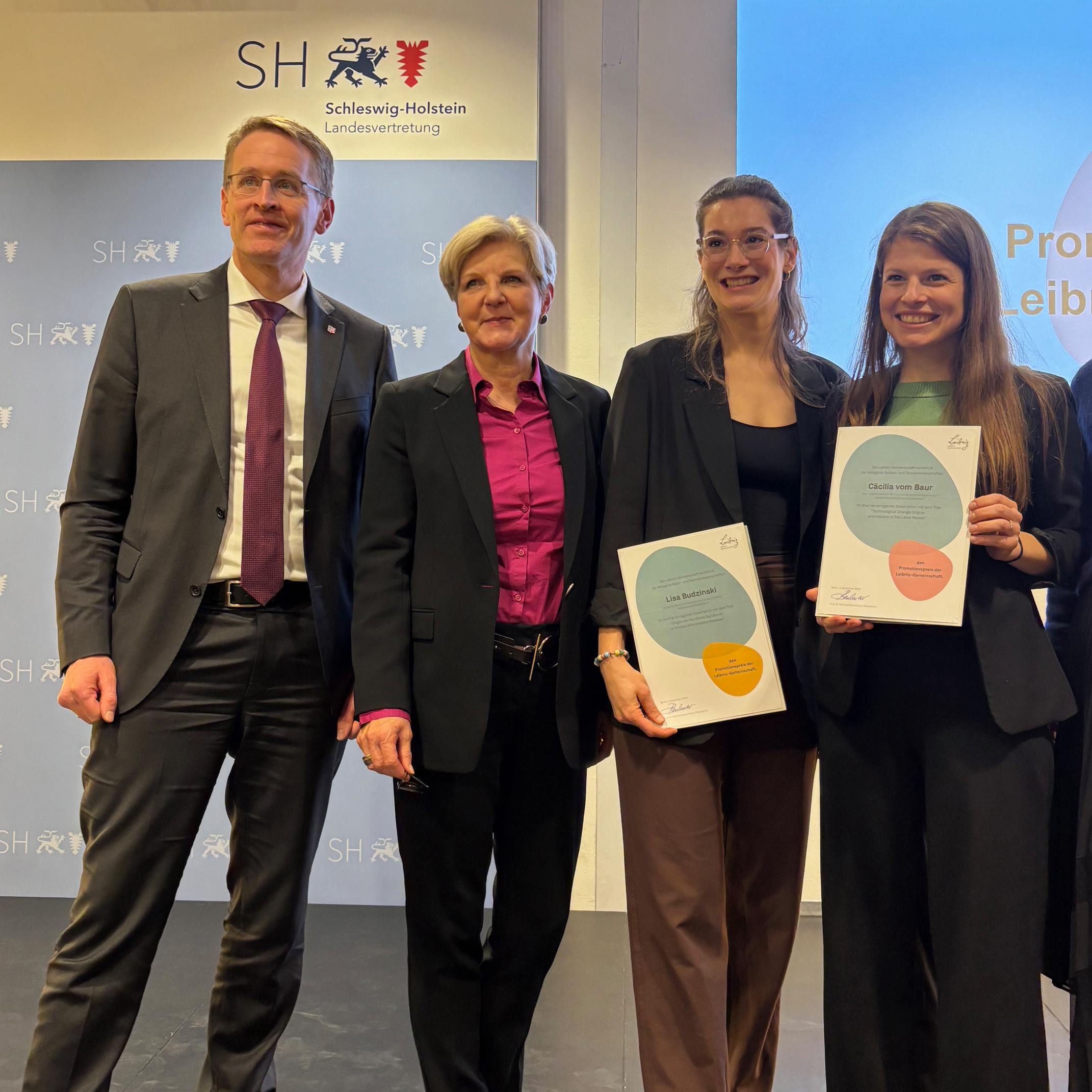 Schleswig-Holsteins Ministerpräsident Daniel Günther und Martina Brockmeier, Präsidentin der Leibniz-Gemeinschaft, stehen neben den Preisträgerinnen Lisa Budzinski und Cäcilia vom Baur.