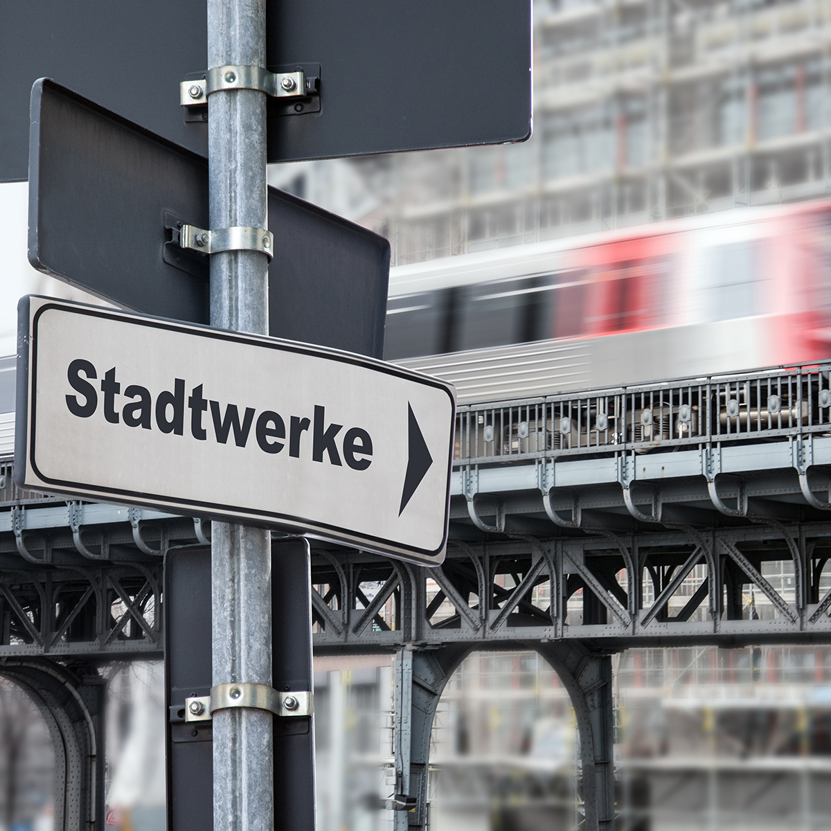 Straßenschild mit Beschriftung "Stadtwerke" und einer vorbeifahrenden Bahn im Hintergrund