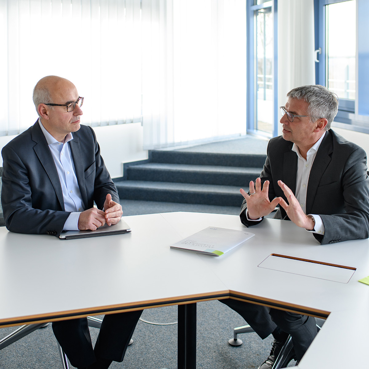 Prof. Achim Wambach, PhD (l.) und Dr. Ralph Rheinboldt sitzen in einem Besprechungsraum.