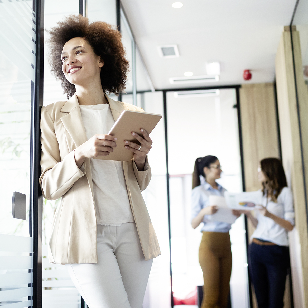 Frau steht mit Tablet in einem Büro und schaut aus dem Fenster.