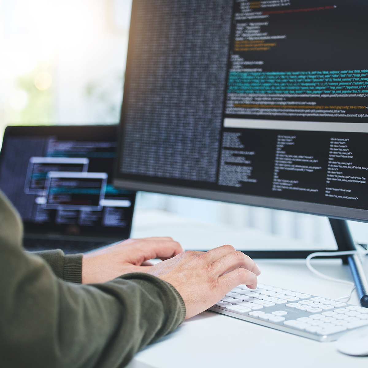 Zwei Hände auf einer Tastatur, darüber ein Monitor mit Programmiercode