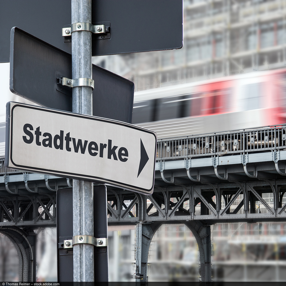 Straßenschild mit Beschriftung "Stadtwerke" und einer vorbeifahrenden Bahn im Hintergrund