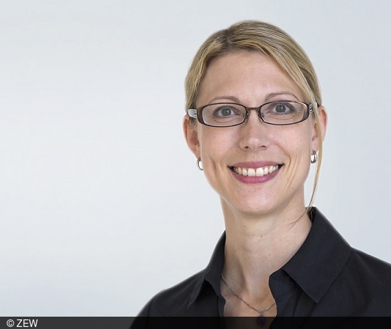 Portraitfoto von Karolin Kirschenmann: Blonde Frau in schwarzer Bluse auf hellgrauem Hintergrund