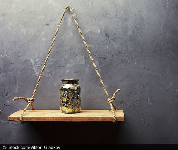 Glas mit Münzen gefüllt steht auf Regalbrett vor Betonwand