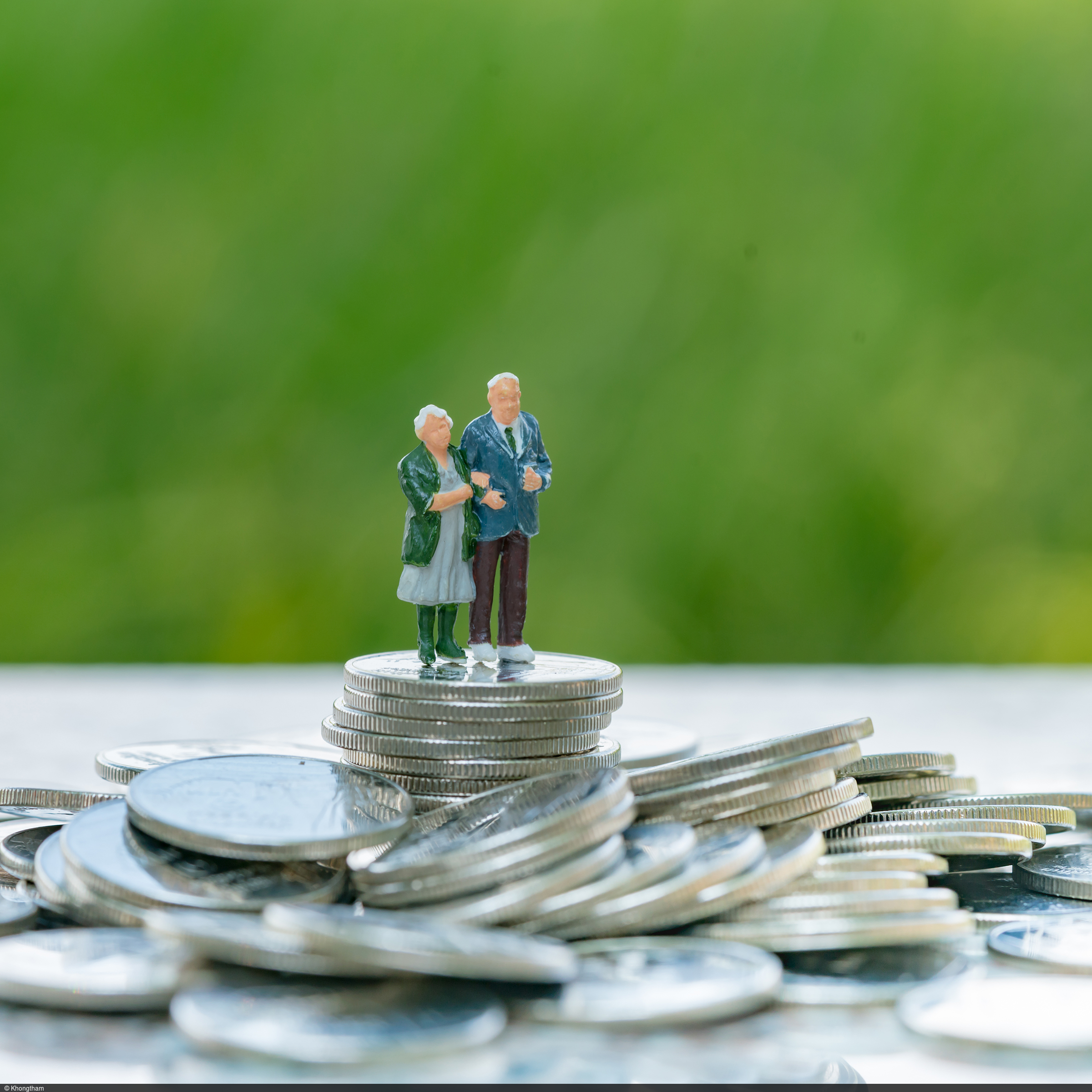 Ein älteres Ehepaar steht vor grünem Hintergrund auf überdimensional großen Münzen