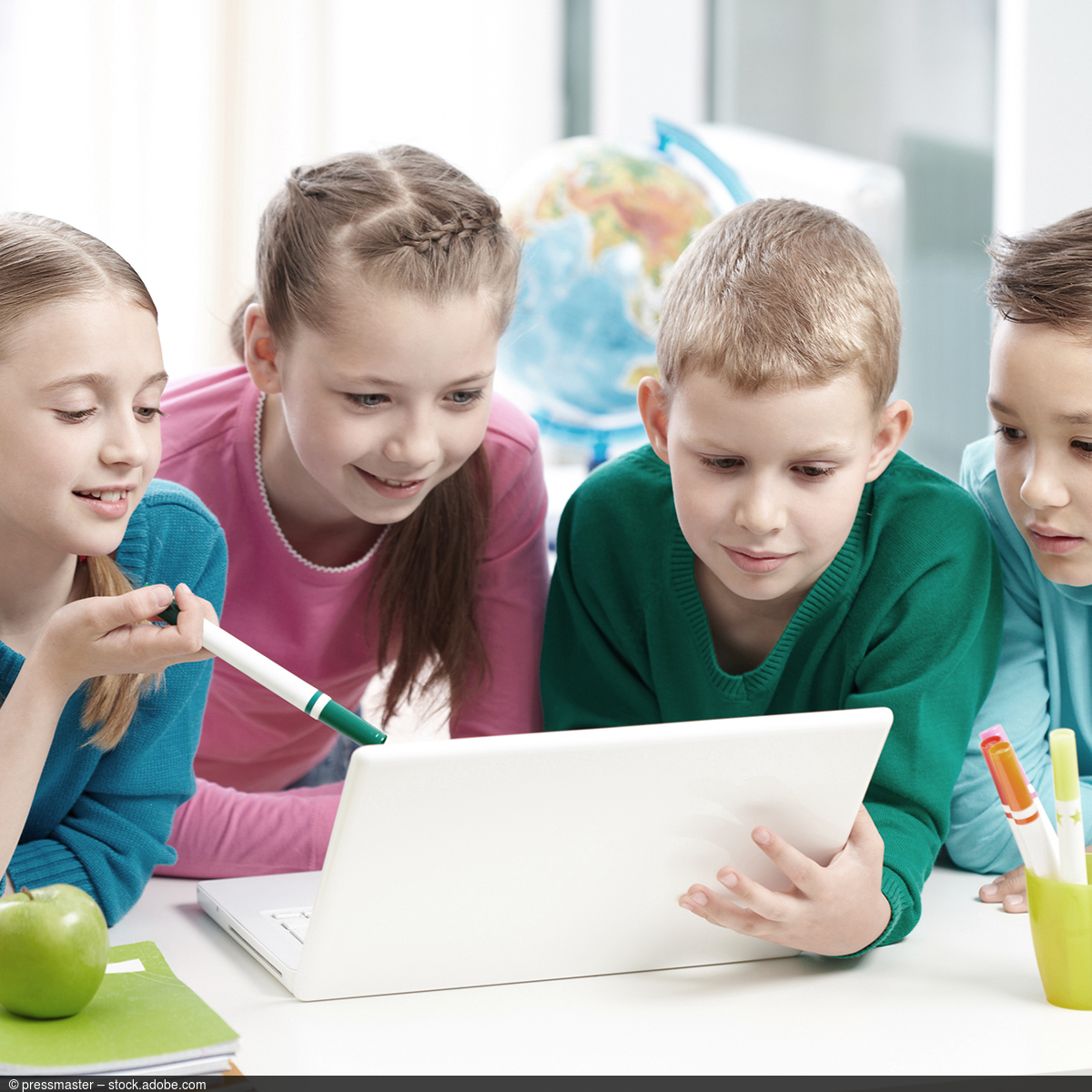 Vier Kinder spielen miteinander und schauen auf einen Laptop