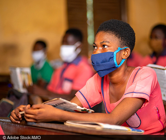 A sub-Saharan school child sits in a classroom wearing a facemask