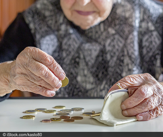 Ältere Frau zählt Bargeld vor sich auf einem Tisch.