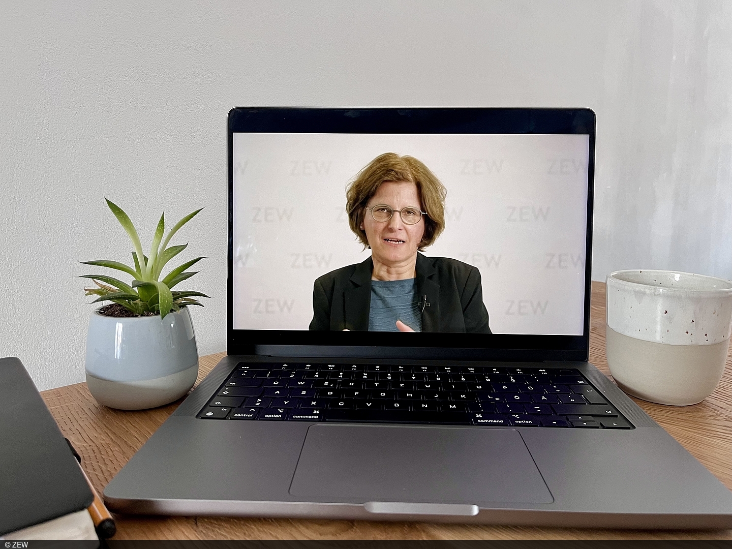 There is a laptop on a wooden table, on whose screen Irene Bertschek can be seen talking.