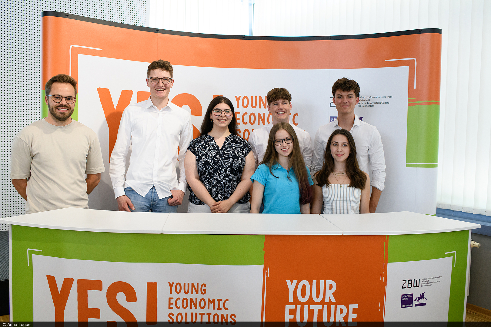 Pupils stand behind a desk with a "YES! Economic Solutions" banner.